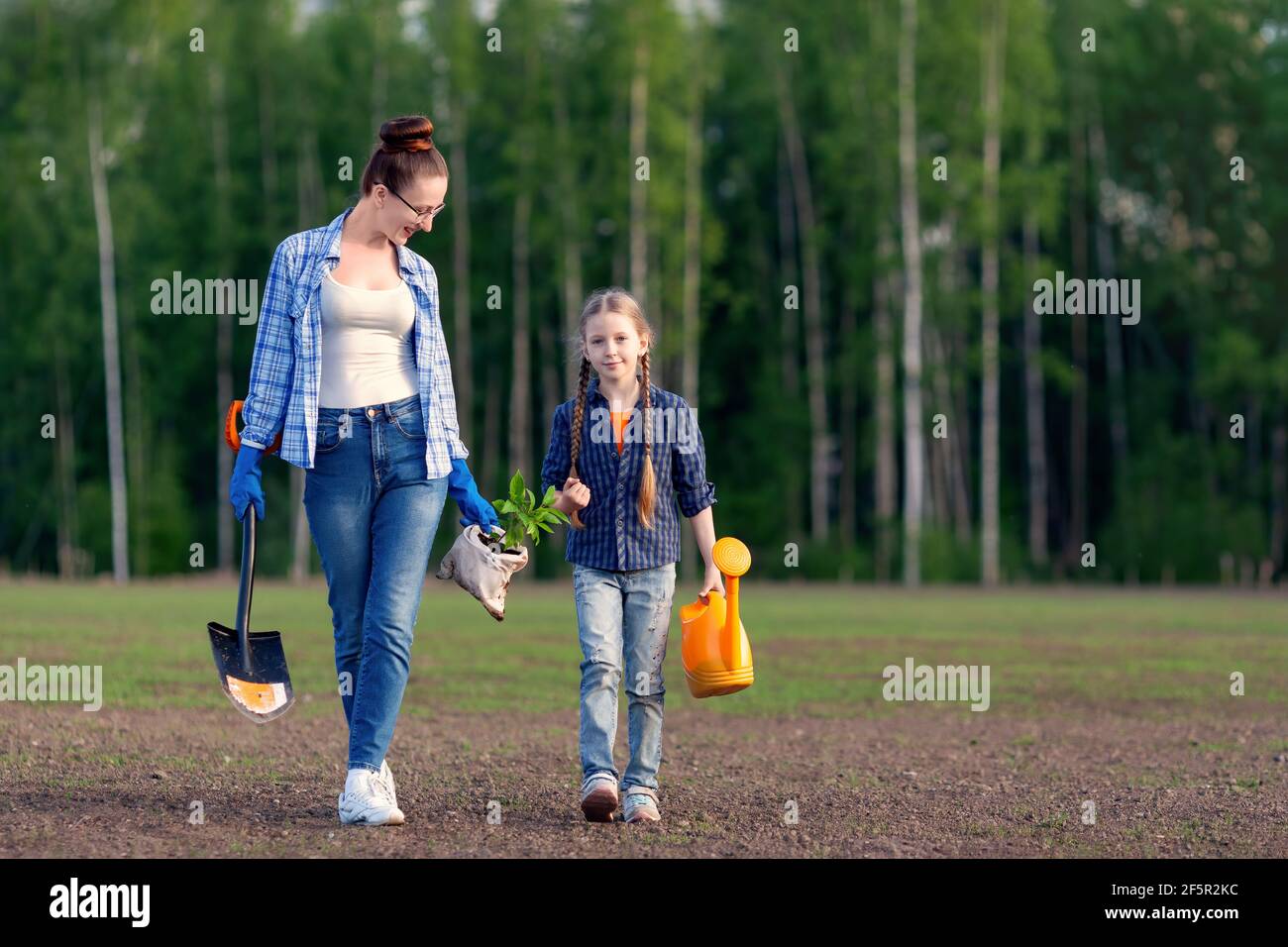 La mère heureuse et la petite fille gamin vont ensemble planter un plantule  d'arbre vert. Les parents apprennent à l'enfant à propos de l'environnement  et de l'éco-soin de la nature. FAM Photo