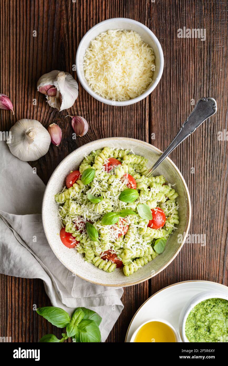 Pâtes fusilli à la sauce pesto au basilic et tomates cerises, parsemées de fromage râpé sur fond de bois rustique Banque D'Images