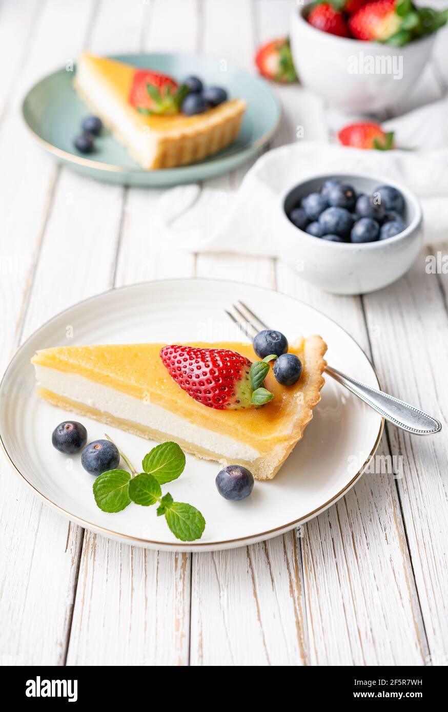 Tranches de tarte au fromage à la crème avec garniture au citron et caillé, servies avec des bleuets frais et des fraises sur fond rustique blanc Banque D'Images
