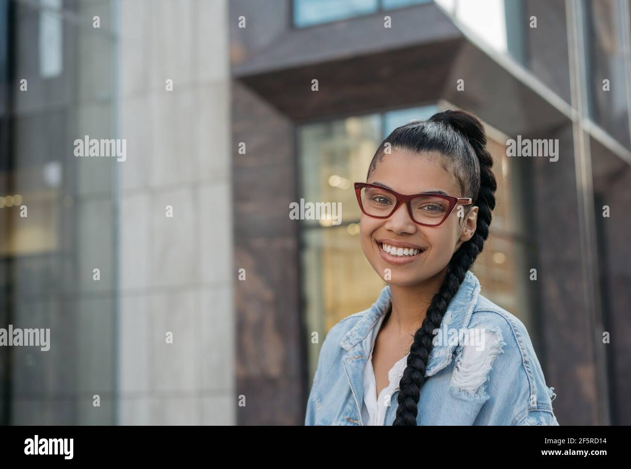 Belle femme afro-américaine portant des lunettes élégantes, debout dans la rue et souriante Banque D'Images