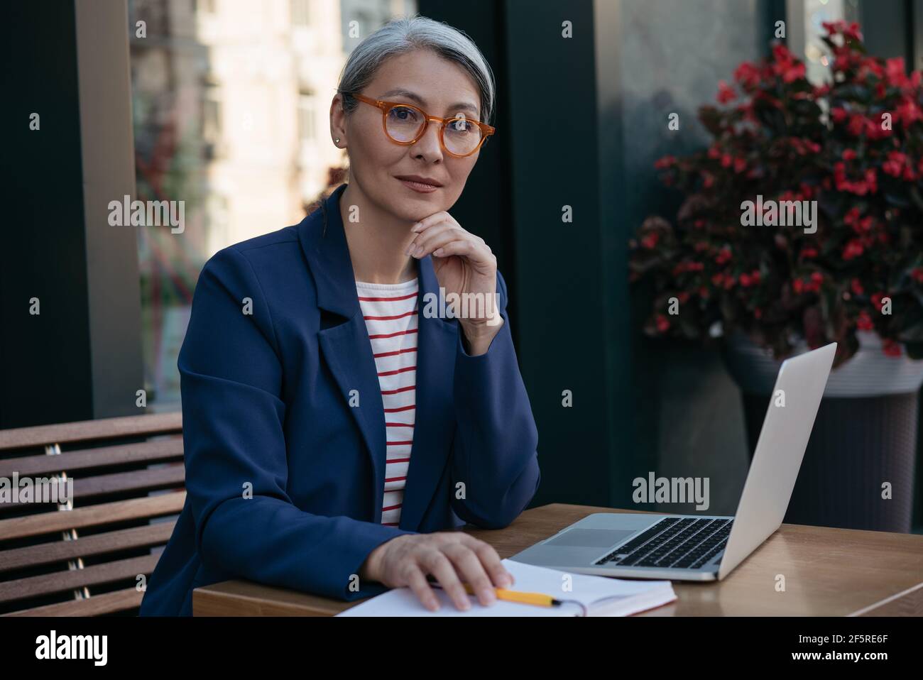 Femme d'affaires pensive et mûre regardant la caméra, assise sur le lieu de travail. Beau travailleur indépendant d'âge moyen, utilisant un ordinateur portable, projet de planification Banque D'Images