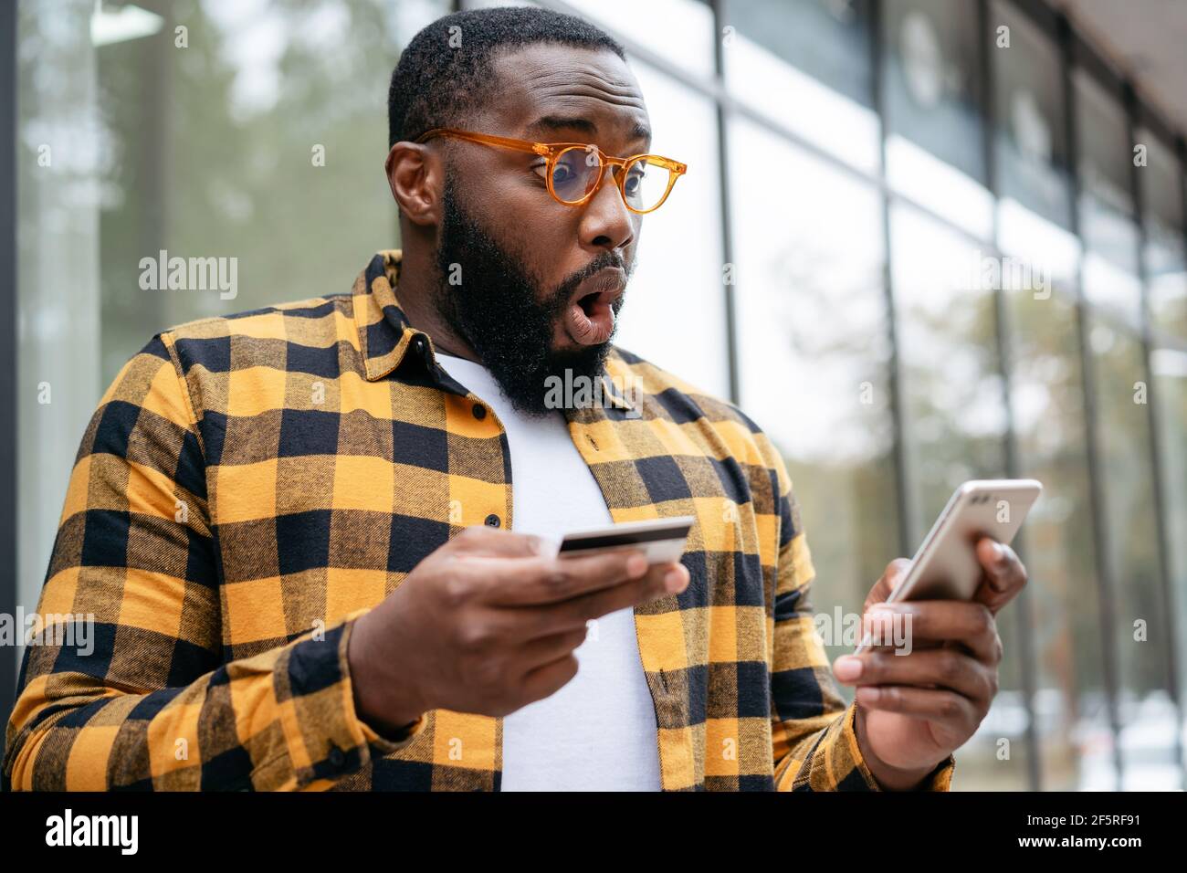Homme afro-américain enthousiaste tenant une carte de crédit, utilisant l'application mobile pour le shopping en ligne. Un travailleur indépendant émotif reçoit le paiement Banque D'Images