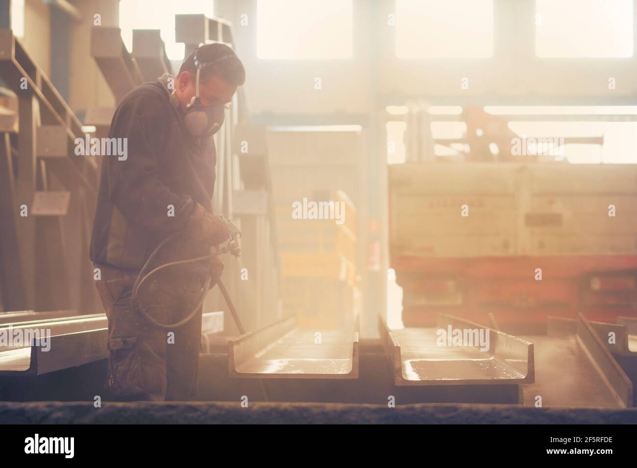Homme peignant de l'acier industriel et laqué avec une machine à compresseur Banque D'Images