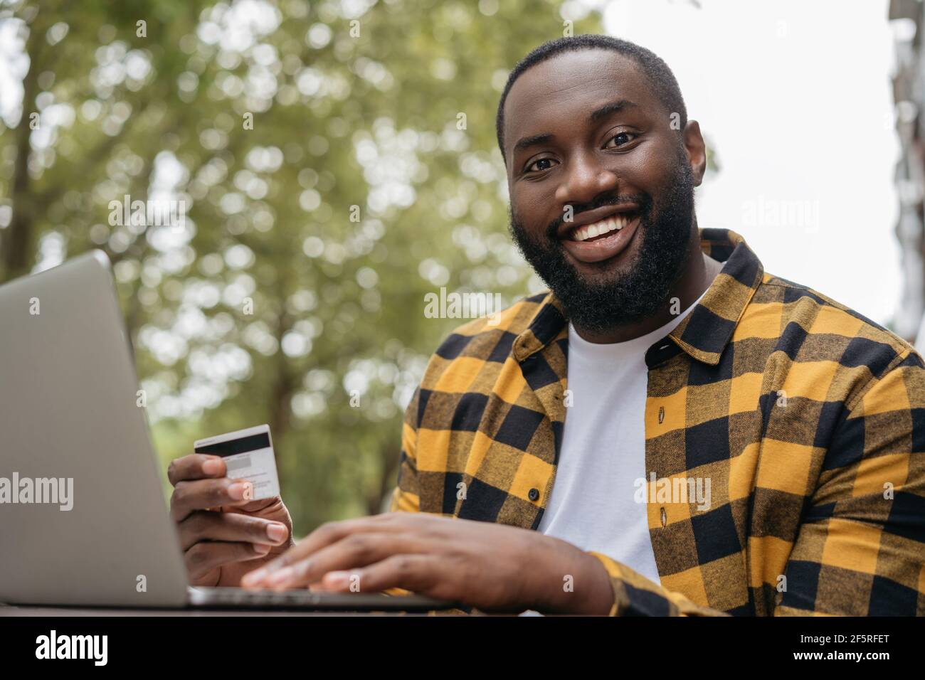 Portrait d'un jeune homme afro-américain souriant tenant une carte de crédit, magasiner en ligne. Concept du Vendredi fou. Bonne réussite freelance recevoir le paiement Banque D'Images