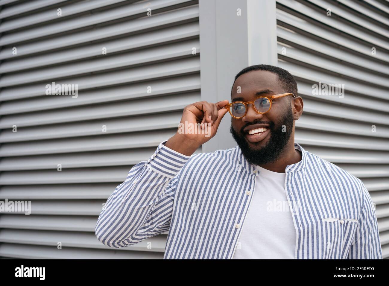 Portrait d'un homme africain souriant et confiant portant des lunettes élégantes isolées sur fond gris Banque D'Images