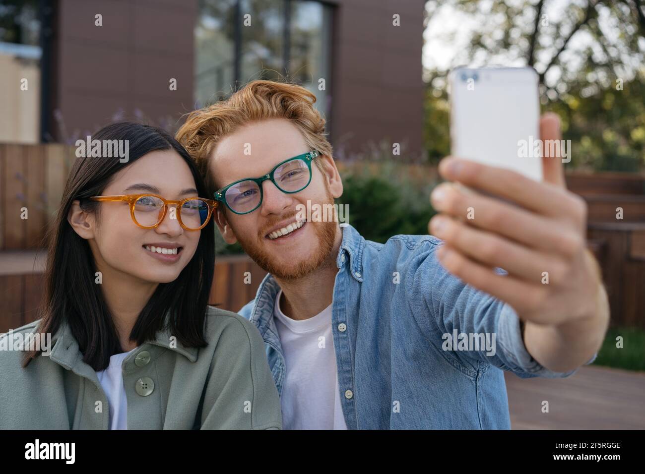 Heureux souriant amis influenceurs à l'aide d'un téléphone mobile, enregistrement vidéo à l'extérieur. Femme et homme rouge portant des lunettes élégantes prenant le selfie Banque D'Images