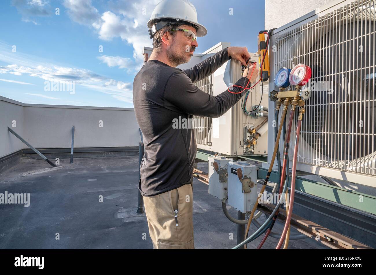 Un technicien HVAC examine la lecture de son multimètre tout en testant la tension d'un mini-système de climatisation divisé. Banque D'Images