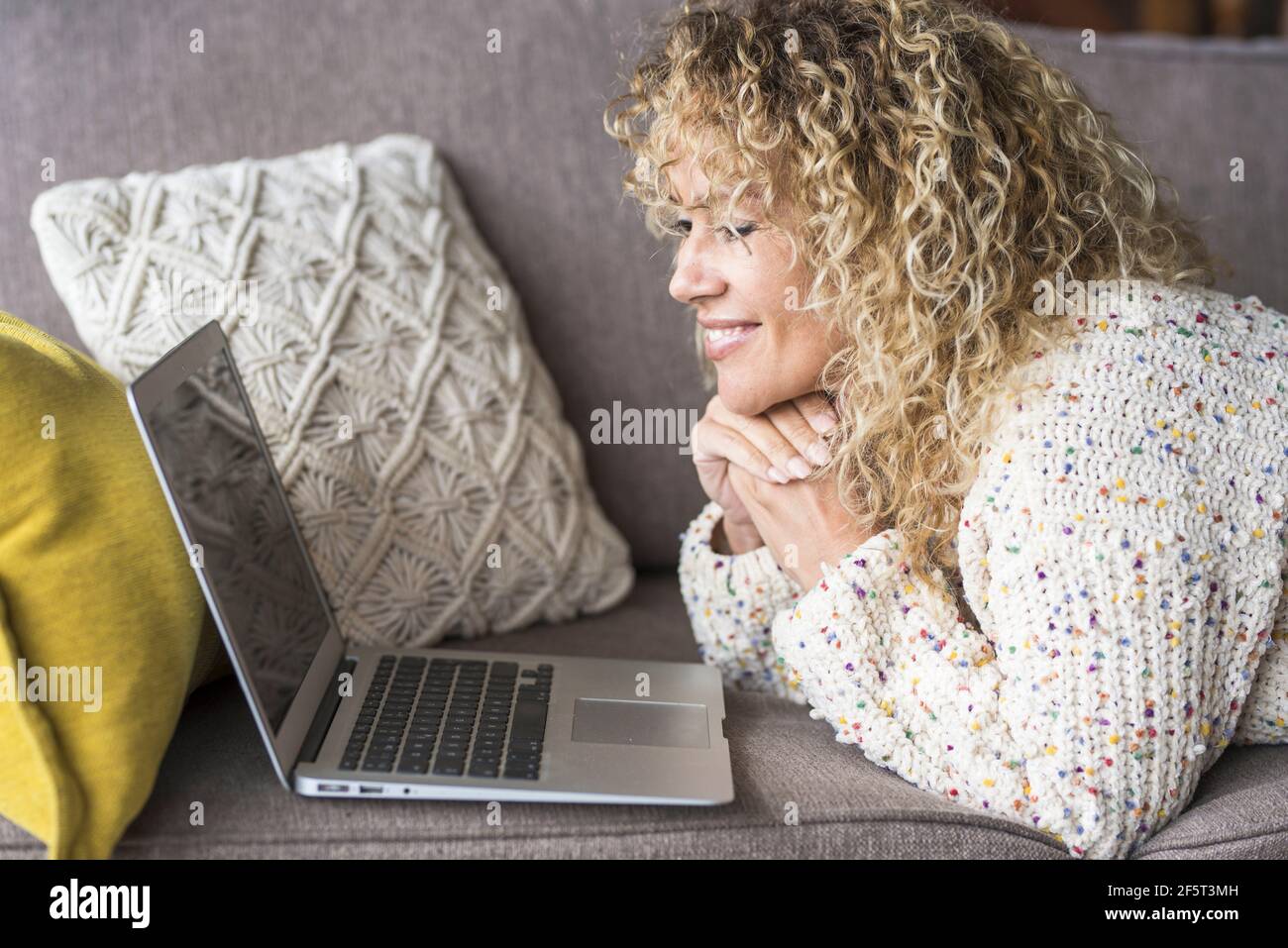 Une femme adulte s'est couché à la maison et se détend avec ordinateur portable : les utilisateurs et les appareils à la maison la vie et le séjour confortables - caucasien f Banque D'Images