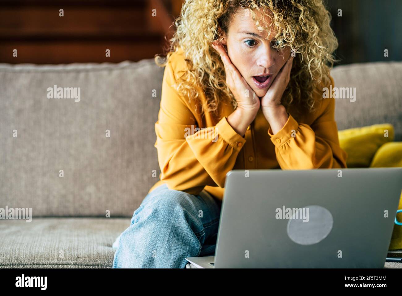 Une femme souriante assise à la maison sur le canapé lisant un message en regardant l'écran de l'appareil à l'aide d'un ordinateur. Une femme excitée se sent satisfaite de l'émotion positive Banque D'Images