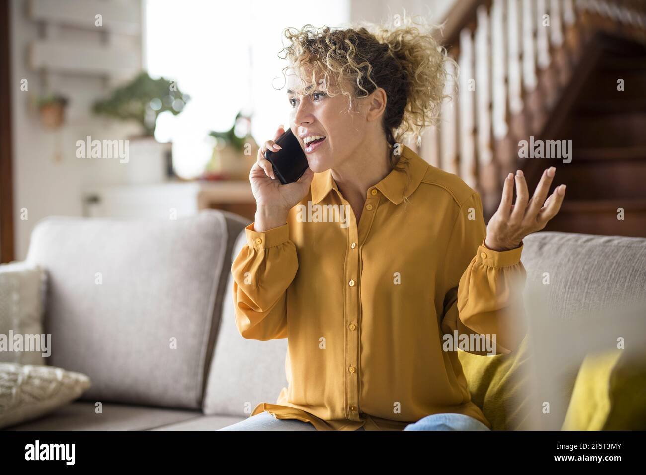 Une femme adulte heureuse à la maison dans le téléphone appelant sourire et profitez d'un moment de loisirs à l'intérieur assis sur le canapé style de vie décontracté - âge moyen élégant pe Banque D'Images