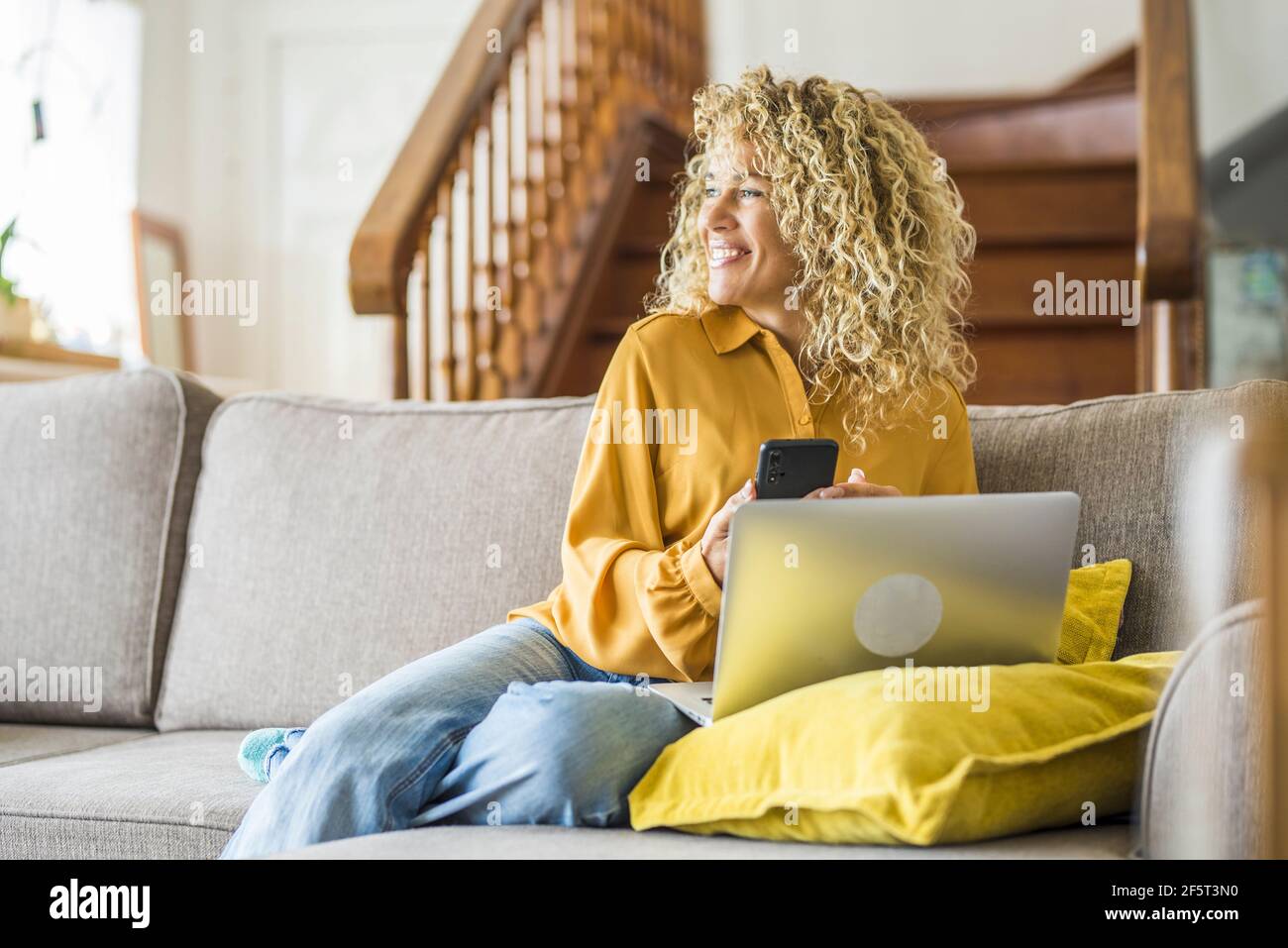 Souriante adulte jeune femme s'assoir se détendre sur le canapé en utilisant l'ordinateur portable moderne de navigation Internet sans fil illimité, heureux jeunes indépendants travail sur ordinateur Banque D'Images