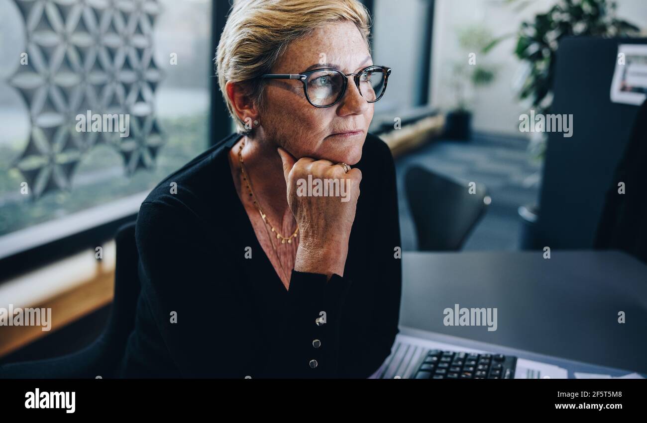 Femme d'affaires senior attentionnés avec main sur le menton au bureau. Femme professionnelle à la recherche et à la réflexion. Banque D'Images