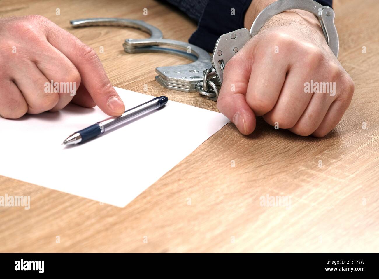 Un détenu au poste de police. Une main est menottée, l'autre est non  boutonnée, et il y a un stylo dans sa main pour écrire des explications.  Arrestation, mise en liberté sous