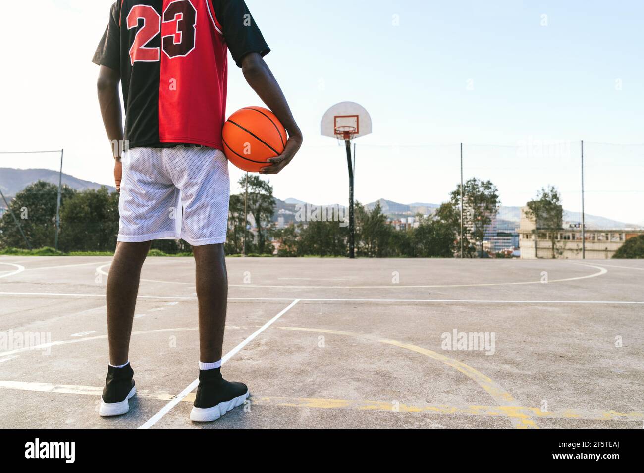 Vue arrière courte d'un joueur de streetball afro-américain méconnaissable en uniforme debout avec ballon sur le terrain de basket-ball Banque D'Images