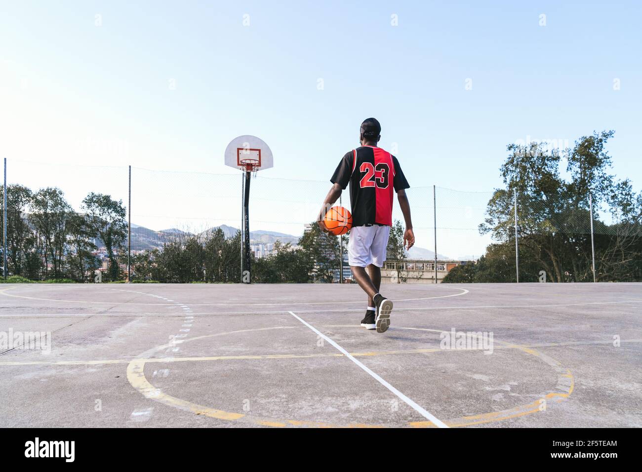 Vue arrière d'un joueur de streetball afro-américain méconnu uniforme avec ballon sur le terrain de basket-ball Banque D'Images