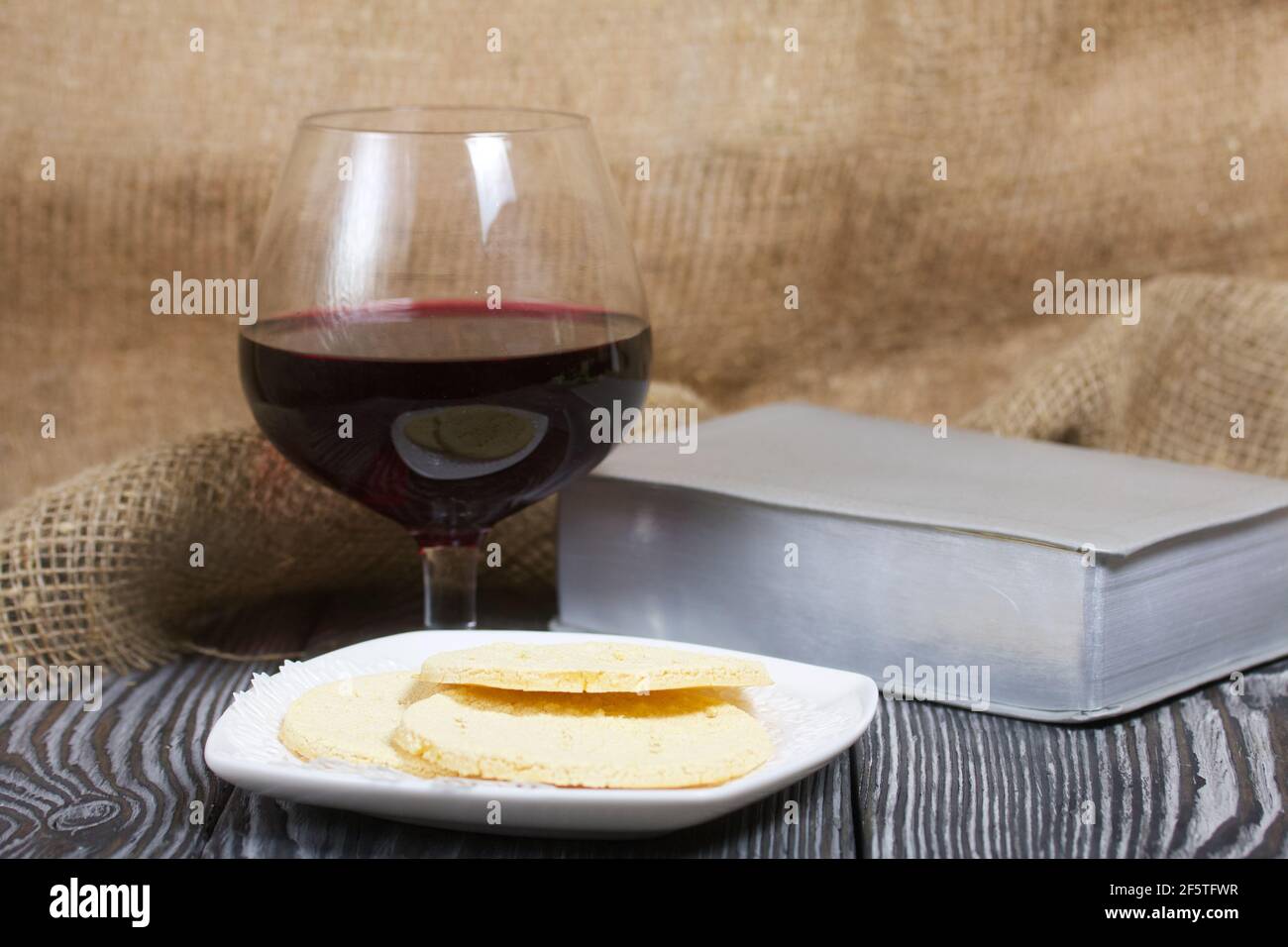 Un verre de vin rouge sec et du pain sans levain cassé se trouvent sur une assiette. Pour célébrer le dîner du Seigneur. À proximité se trouve la Bible. Banque D'Images