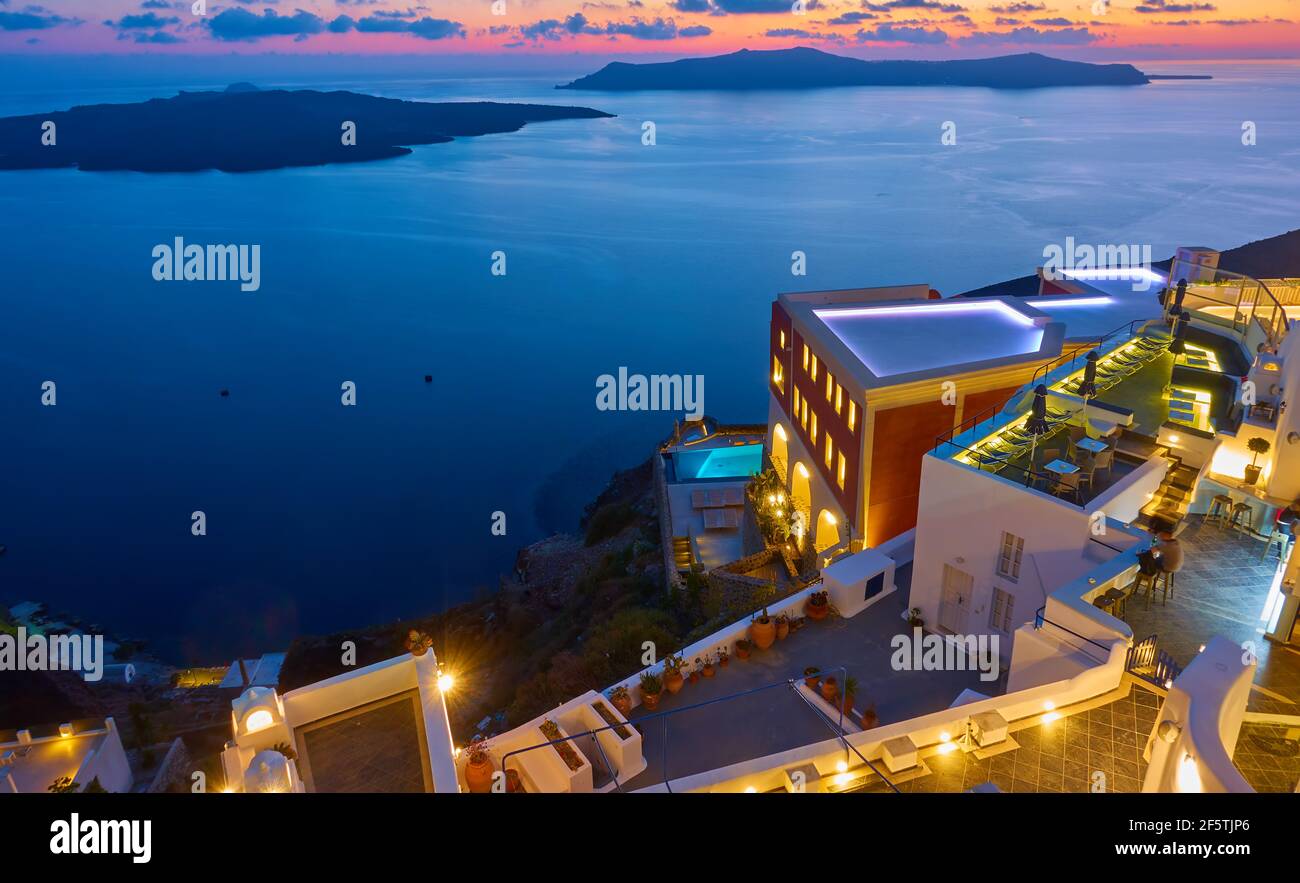 Vue panoramique avec bâtiments éclairés sur la côte de l'île de Santorin et mer Égée au crépuscule, Fira, Grèce. Paysage Banque D'Images