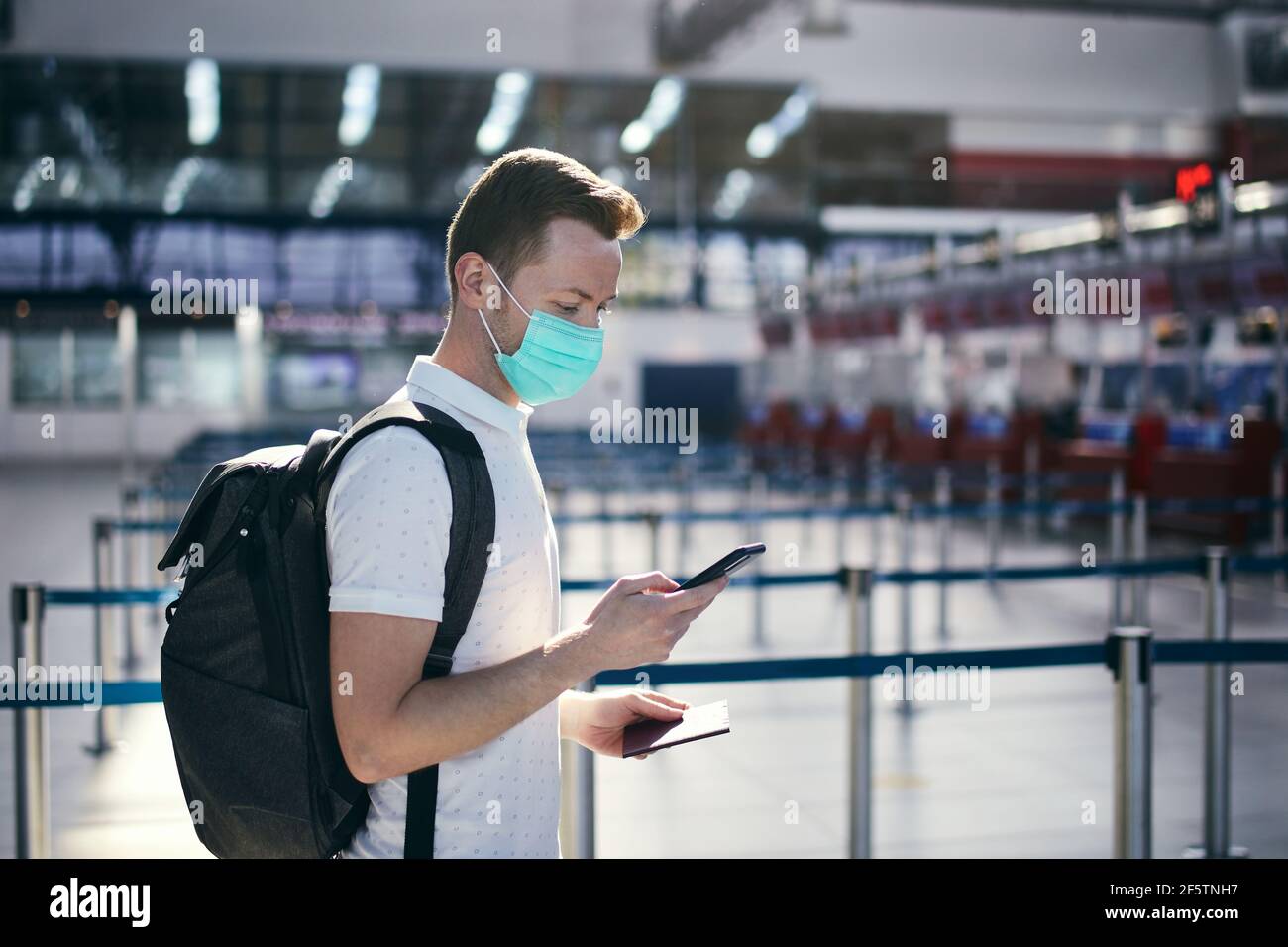 Se déplacer dans la nouvelle norme. Homme utilisant l'application mobile à l'aéroport. Passager portant un masque et tenant un smartphone avec un passeport. Banque D'Images