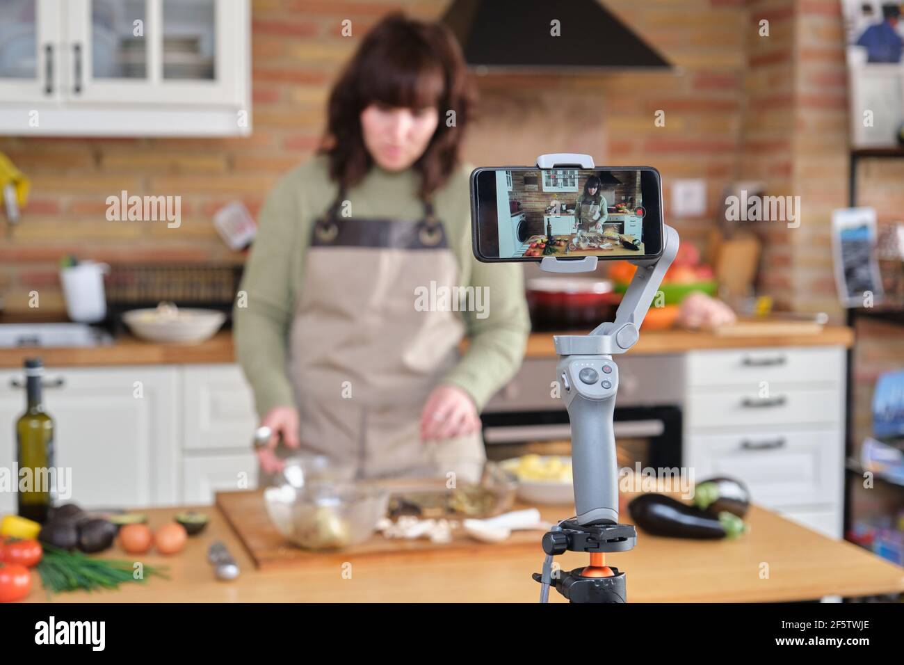 Jeune femme expliquant comment cuisiner des aubergines farcies et enregistrer une vidéo avec son smartphone pour sa chaîne de cuisine. Créateur de contenu et influence Banque D'Images
