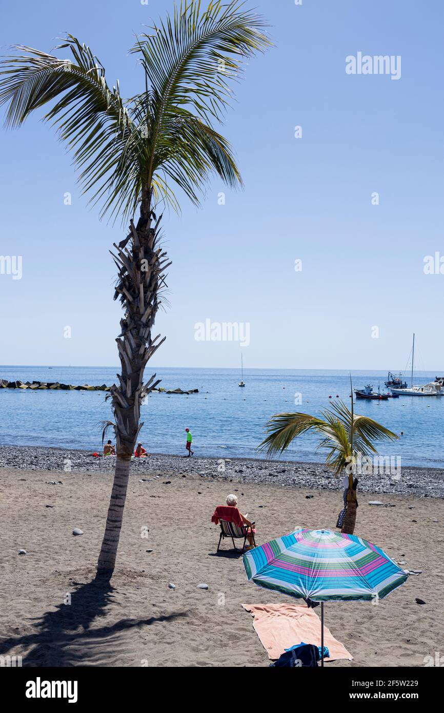 Peu de personnes sur la plage par des palmiers et un parasol et une serviette sur le sable à Playa San Juan, Tenerife, îles Canaries, Espagne Banque D'Images