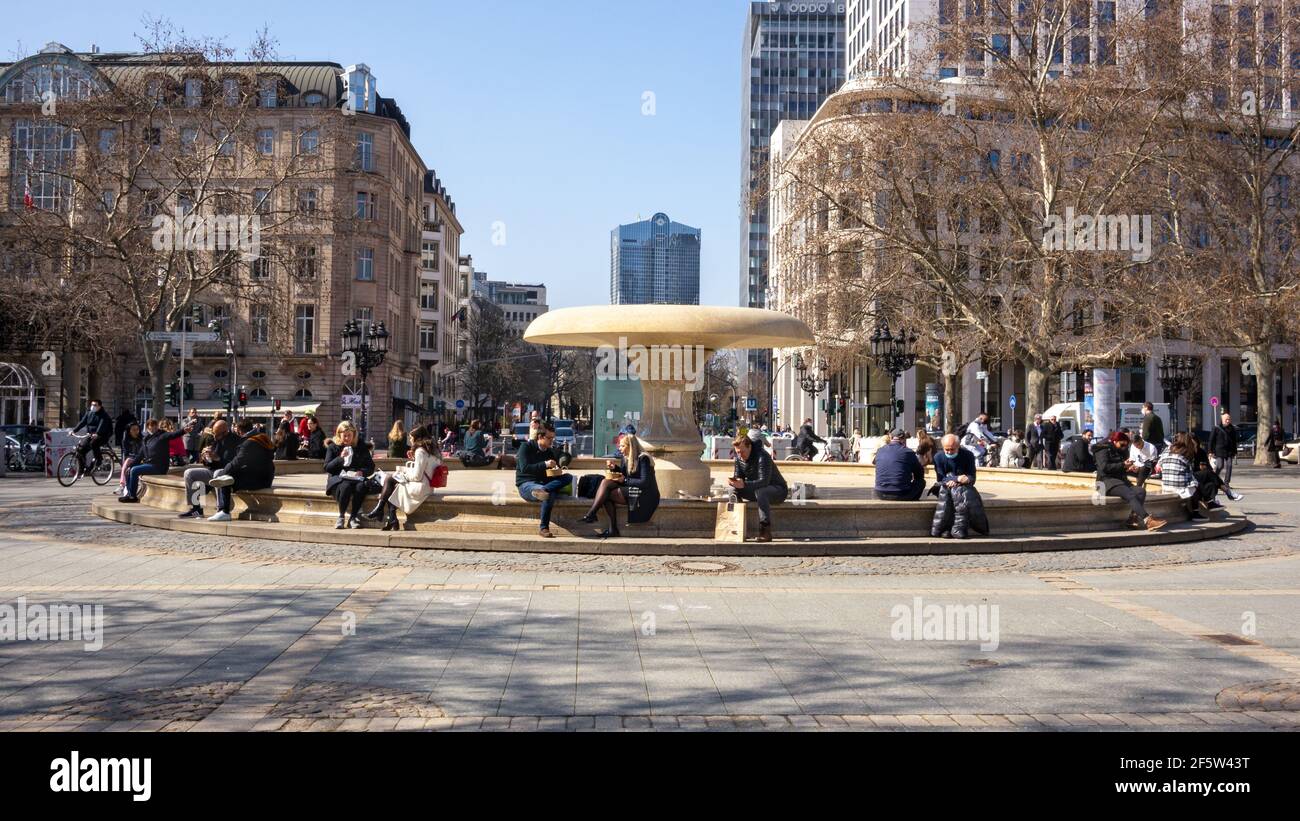 Les gens s'assoient à l'extérieur sur la frontière de la fontaine avec la distance, avec des plats à emporter dans la pause déjeuner, centre financier de la ville, tandis que les restaurants restent fermés. Banque D'Images