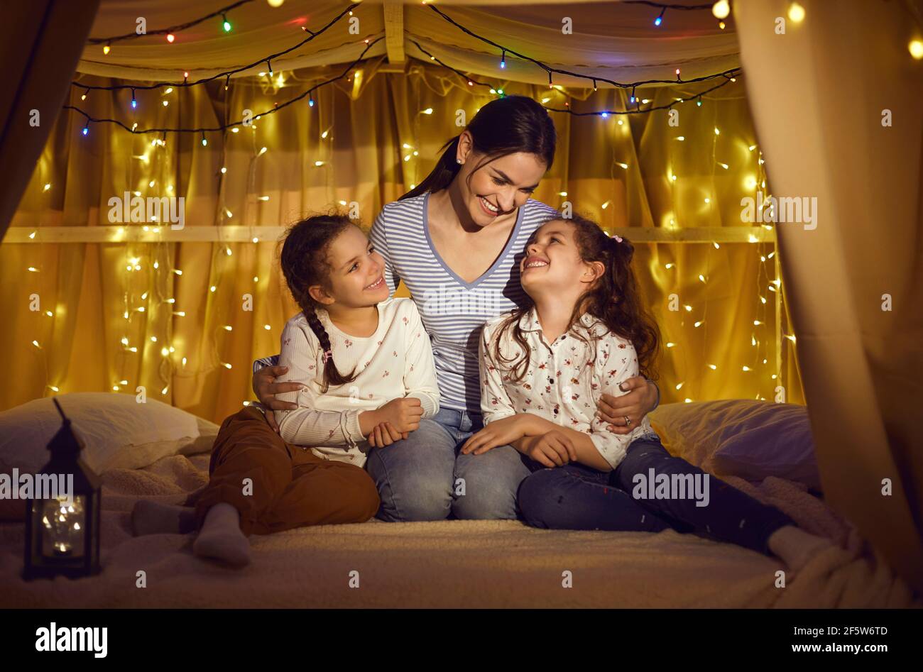 Portrait de la mère embrassant deux petites filles assis dans une tente à la maison Banque D'Images