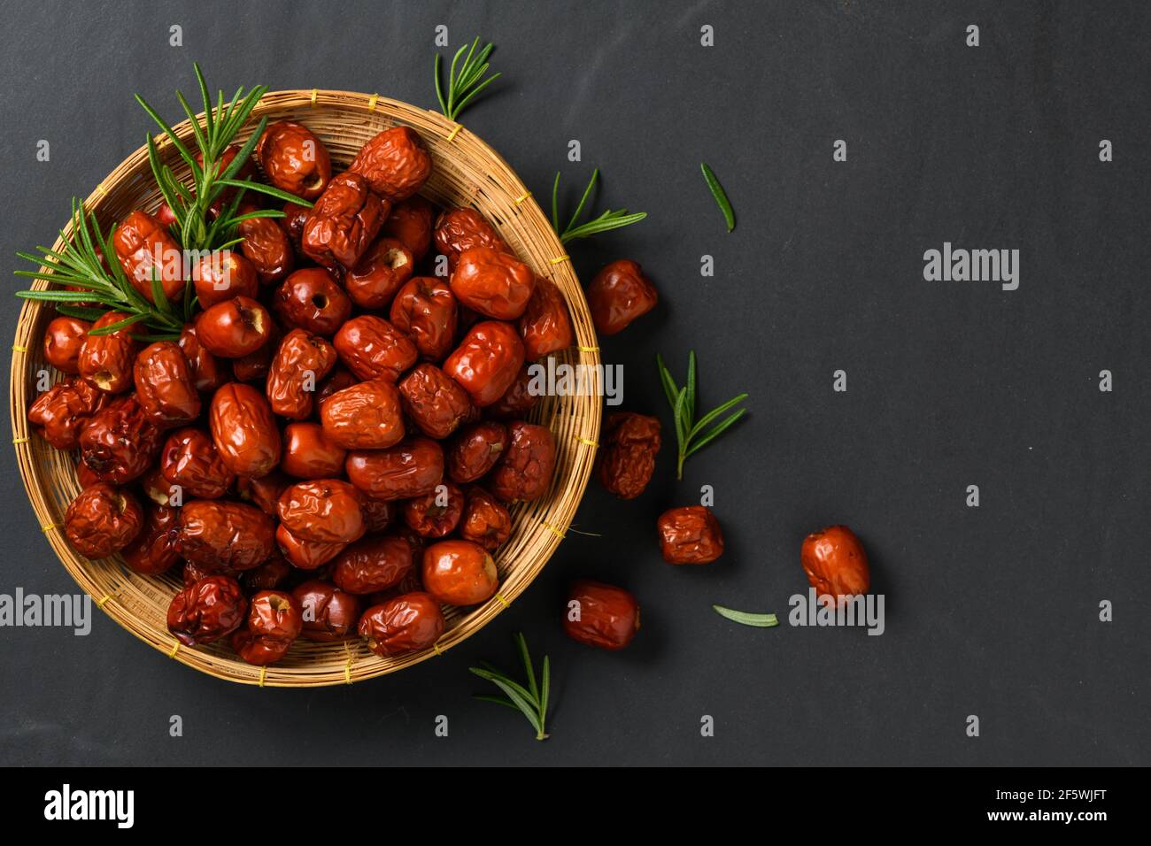 Jujube séché, fruit de datte rouge séché chinois avec feuille de romarin  dans un panier de bambou sur fond noir, fruits à base de plantes. Il a plus  de vitamine C qui