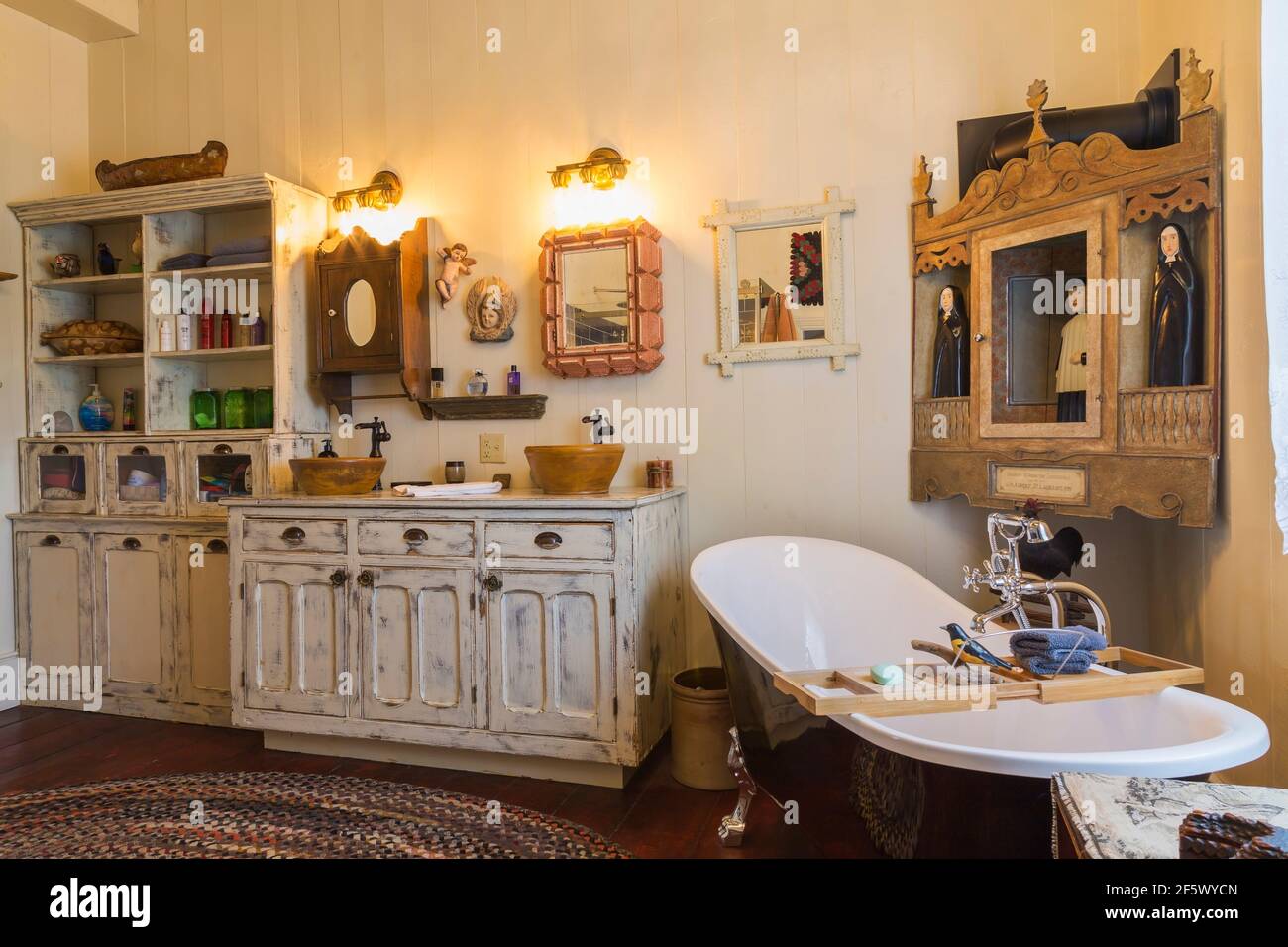 Armoire de magasin générale en bois antique blanchi avec deux bols moulés lavabos et baignoire sur pieds dans la salle de bains principale avec douche tapis ovale multicolore Banque D'Images