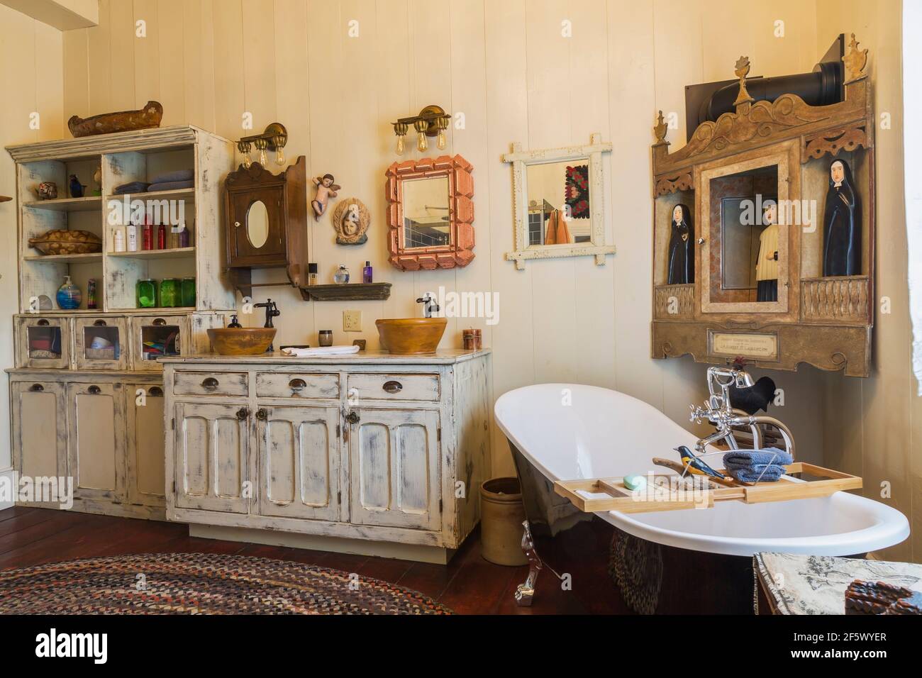 Armoire de magasin générale en bois antique blanchi avec deux bols moulés lavabos et baignoire de pied à griffe noire dans la salle de bains principale avec tapis tissé multicolore Banque D'Images