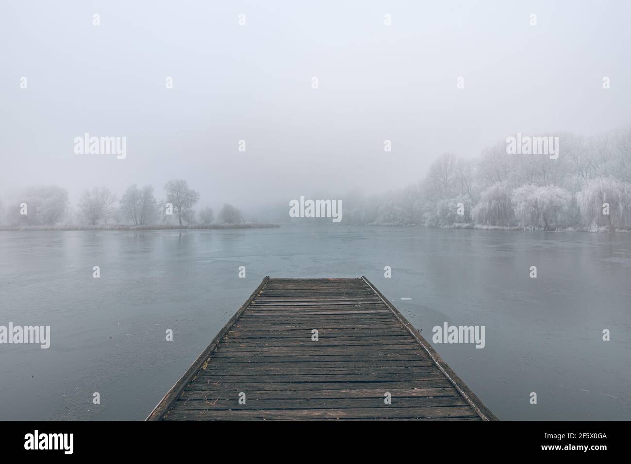 Lac gelé en hiver, avec jetée en bois, et arbres couverts de neige, beau coucher de soleil brumeux sur la forêt. Magnifique paysage d'hiver de saison paisible Banque D'Images
