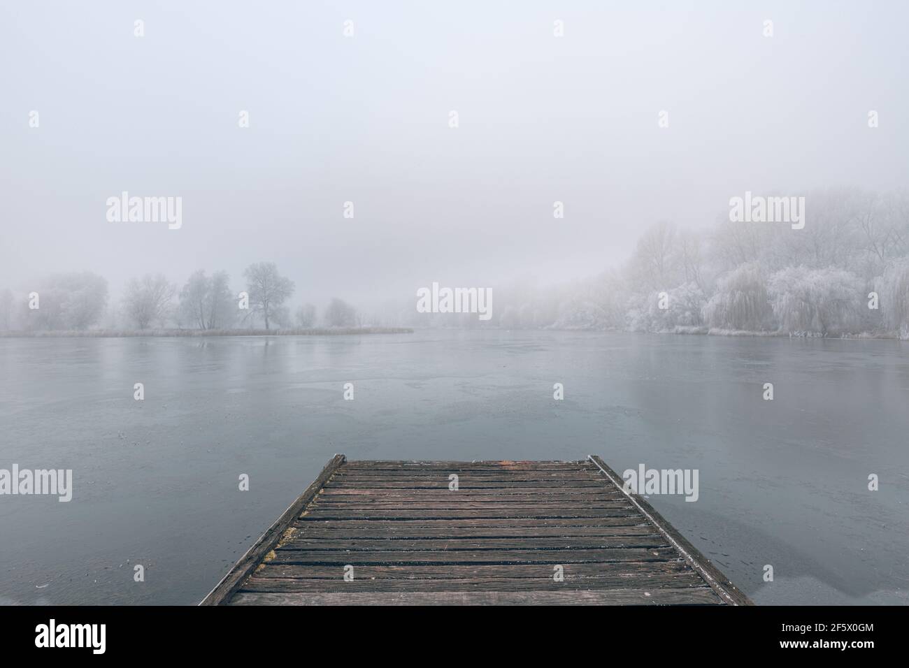 Lac gelé en hiver, avec jetée en bois, et arbres couverts de neige, beau coucher de soleil brumeux sur la forêt. Magnifique paysage d'hiver de saison paisible Banque D'Images
