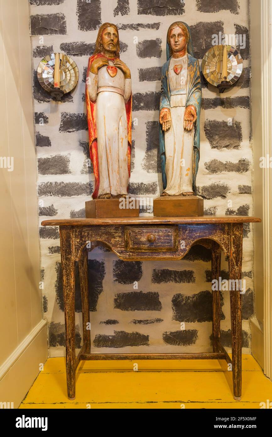 Sculptures religieuses en bois peintes sur une table contre une cheminée en pierre naturelle Mur dans le couloir à l'étage à l'intérieur d'un vieux Canadiana vers 1790 maison de campagne Banque D'Images