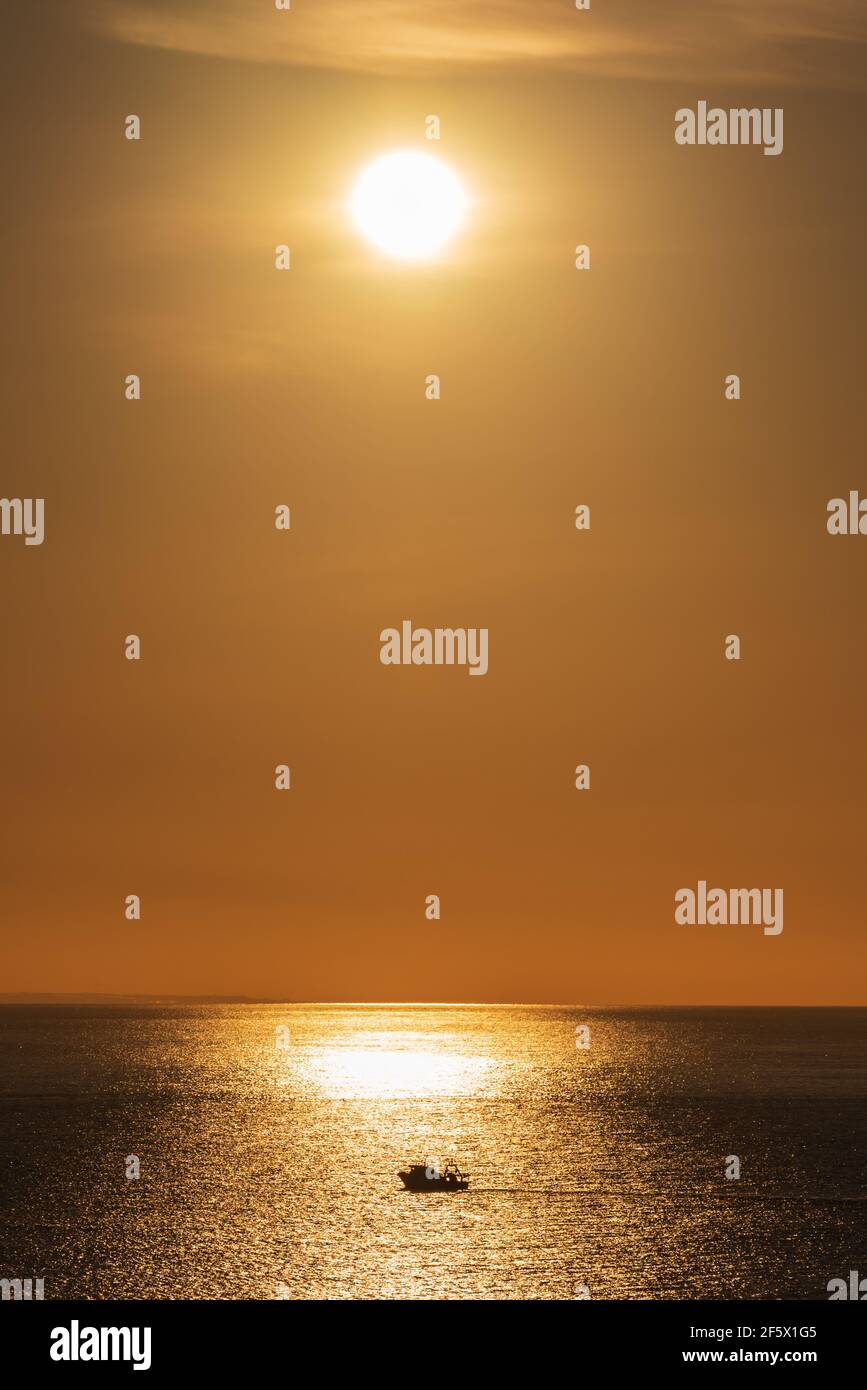 Paysage avec le soleil se reflète dans la mer et la silhouette d'un bateau de pêche sur le reflet. Banque D'Images