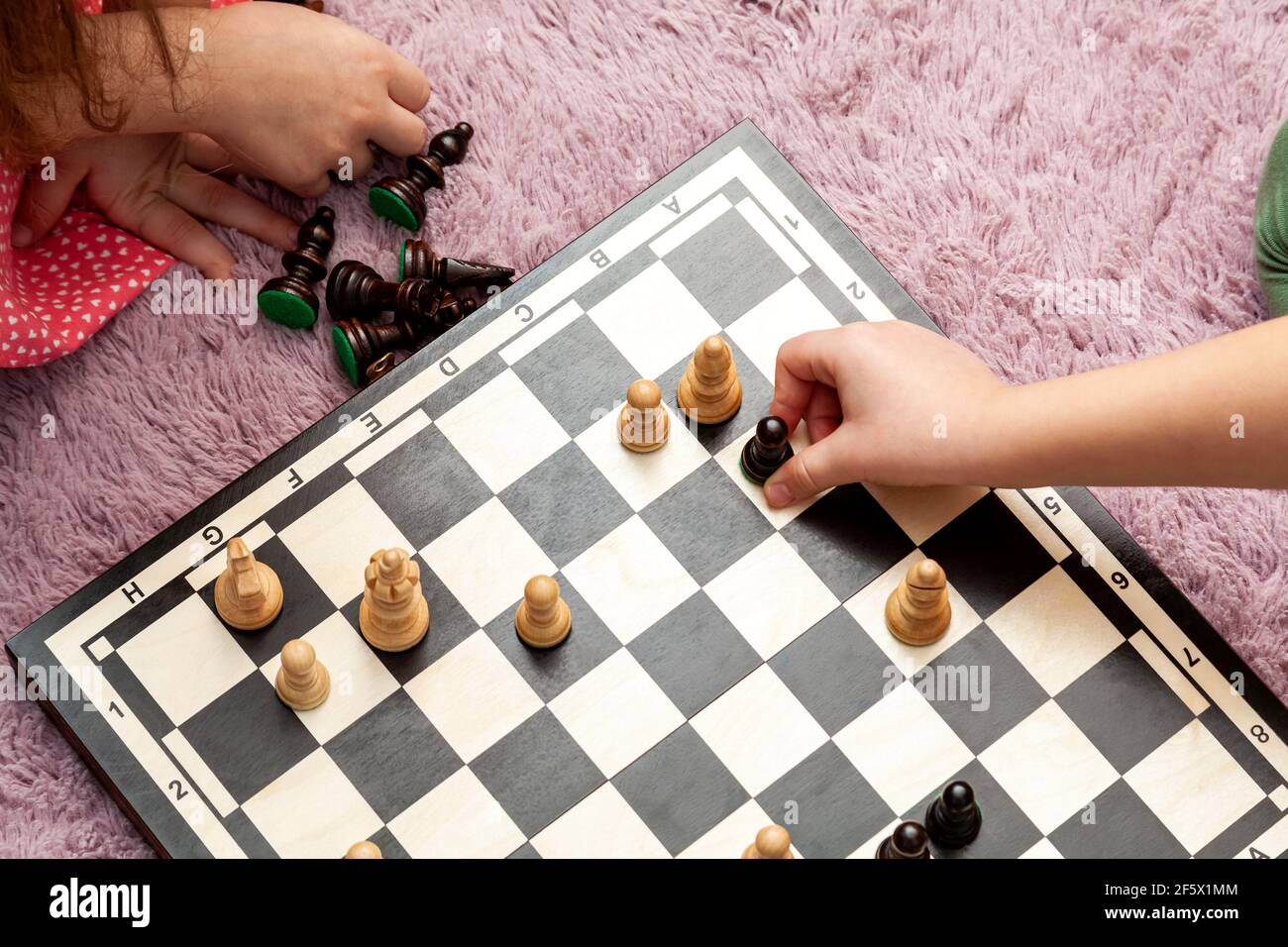 Anonyme jeunes enfants d'âge scolaire jouant aux échecs à la maison, à bord sur le sol, les mains de gros plan, les pièces mobiles d'échecs. Vue de dessus de l'échiquier, simple haut an Banque D'Images