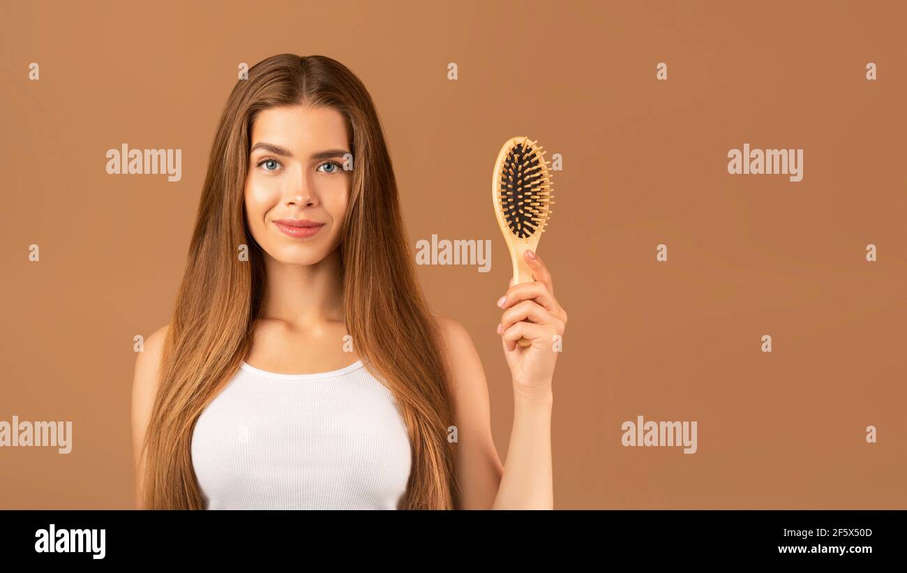Beauté naturelle. Belle jeune femme avec des cheveux longs parfaits tenant une brosse à cheveux en bois sur fond brun studio Banque D'Images