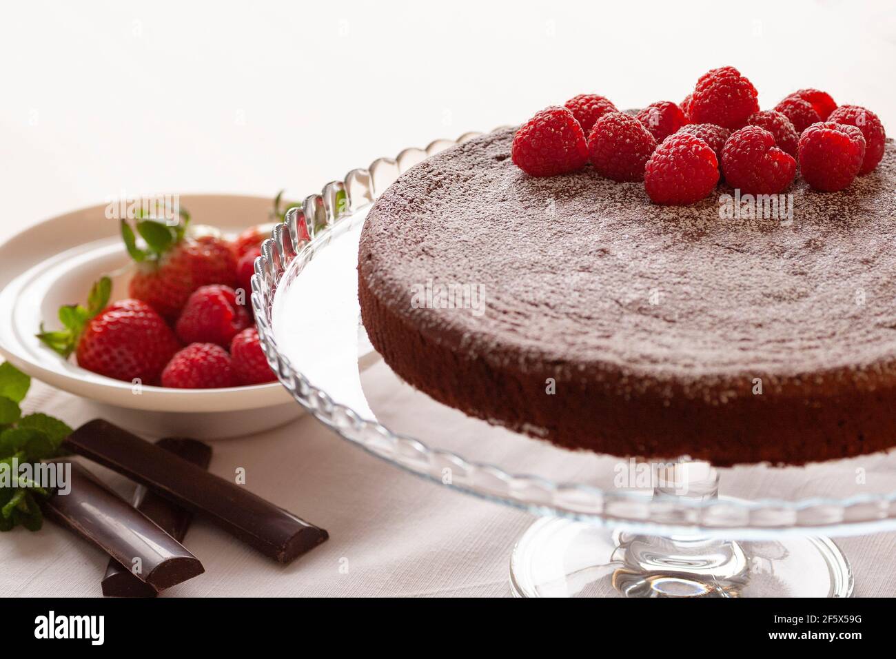 Gâteau au chocolat fait maison servi sur une élégante assiette en verre avec framboises sur le dessus et un bol de fraises à côté il Banque D'Images