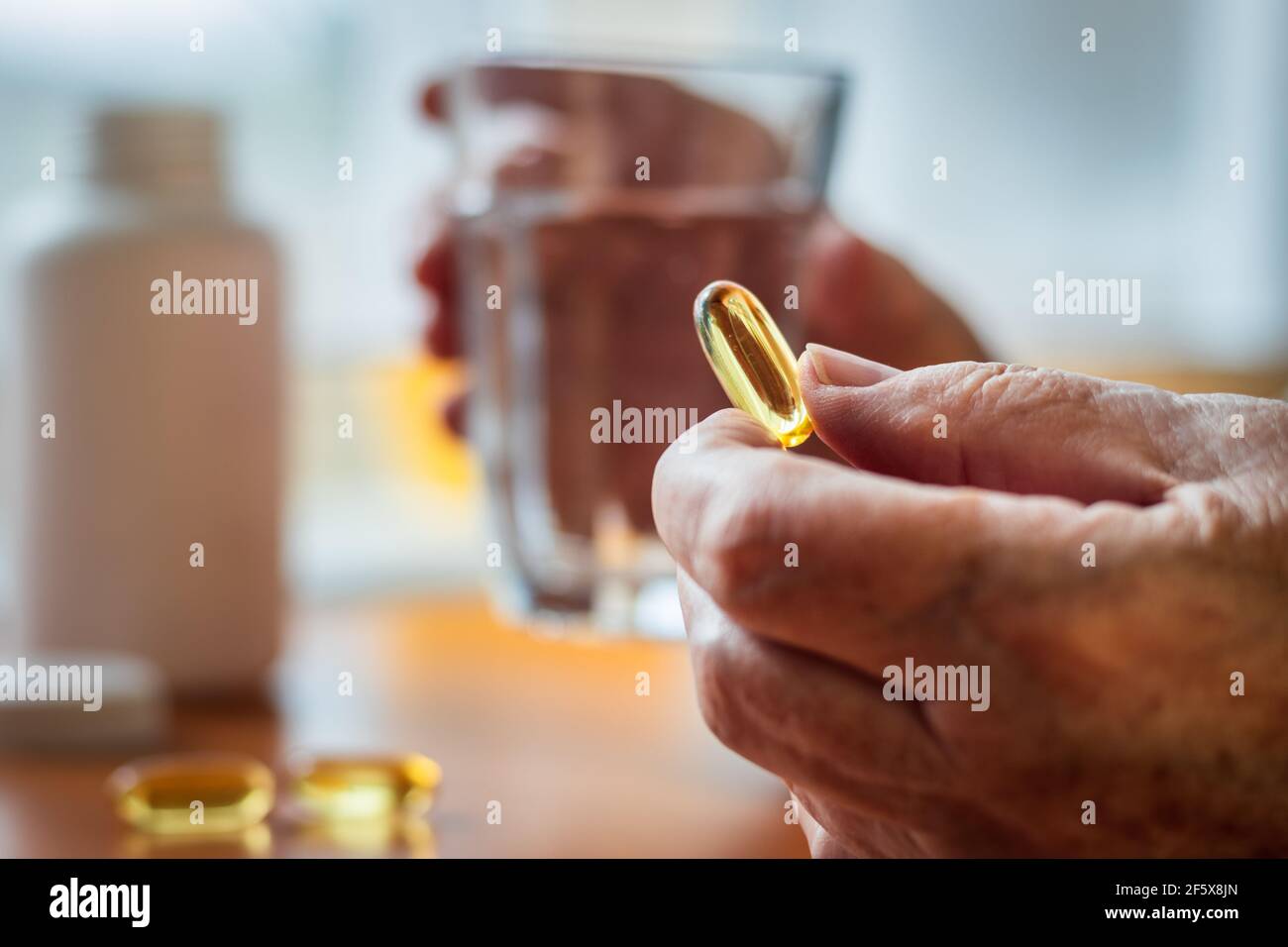 Femme âgée tenant un supplément nutritionnel d'huile de poisson oméga-3 et un verre d'eau dans ses mains. Prise de supplément alimentaire. Santé et concept médical W Banque D'Images