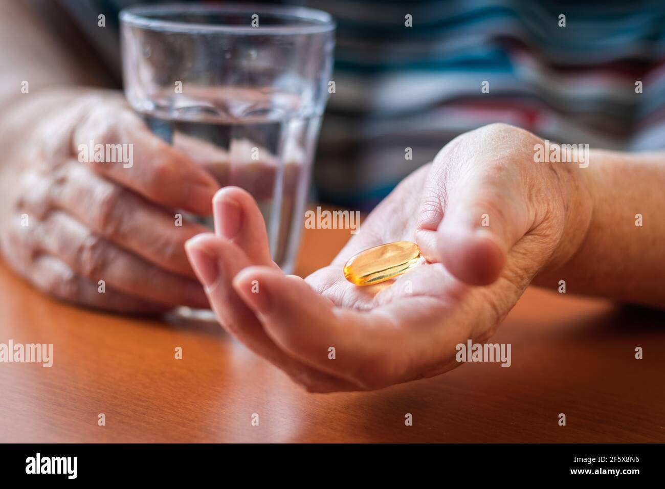 Femme âgée tenant une capsule d'huile de poisson oméga-3 et un verre d'eau dans ses mains. Prise de supplément alimentaire. Santé et concept médical avec les gens Banque D'Images