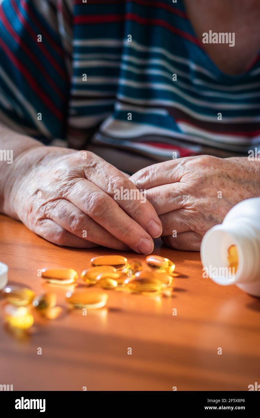 Vieilles mains de femmes et capsule omega-3 sur la table. Femme senior et supplément nutritionnel huile de poisson. Prendre des médicaments pour une bonne santé Banque D'Images