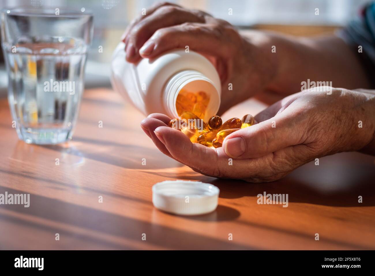 Femme âgée prenant des pilules omega 3 de la bouteille. Santé et concept médical avec les gens. Mains de femmes, supplément alimentaire et verre d'eau Banque D'Images