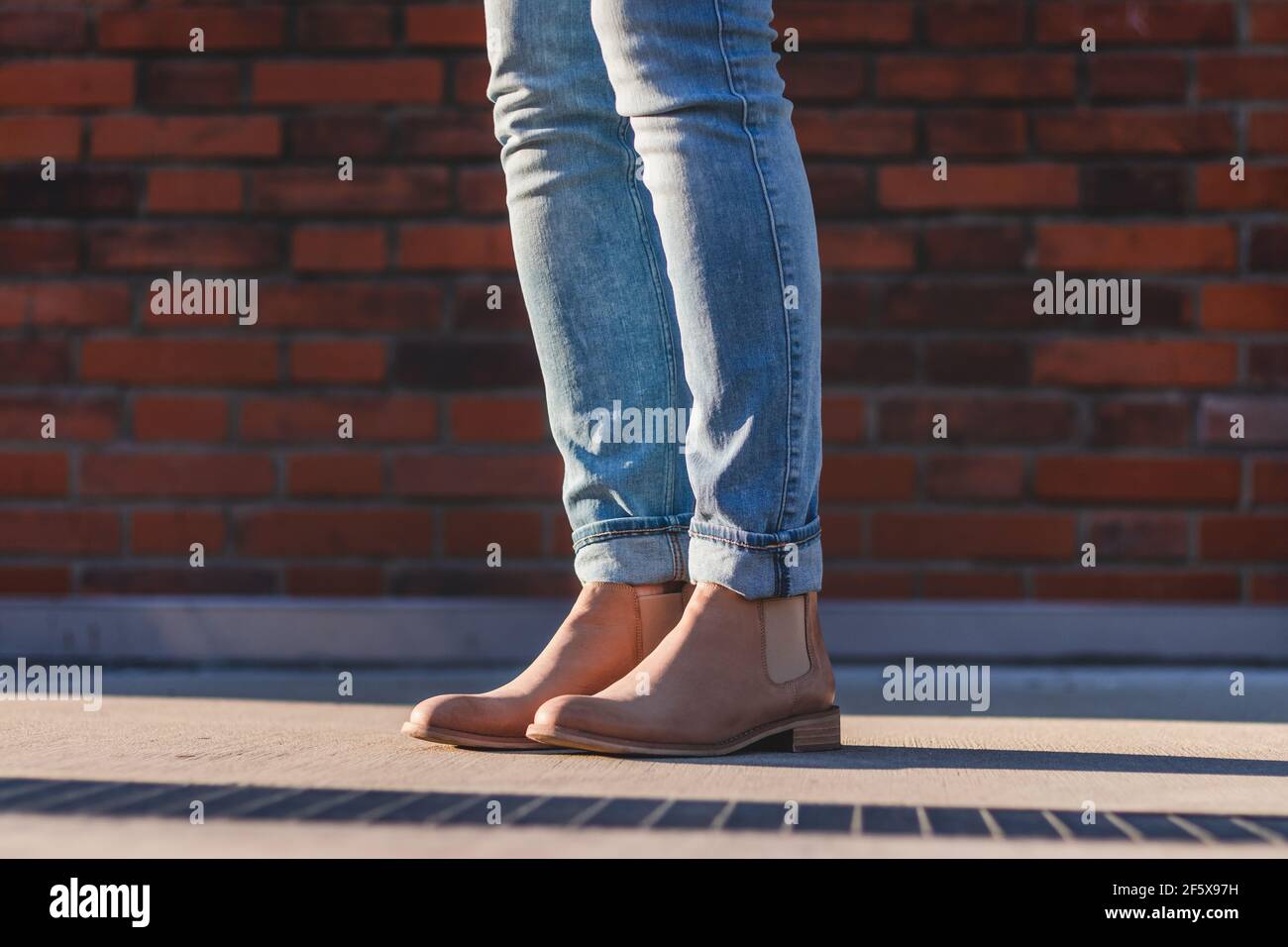 Les jambes des femmes portant un Jean et une botte de cuir se tenant près du mur de briques. Femme portant des vêtements décontractés en ville Banque D'Images