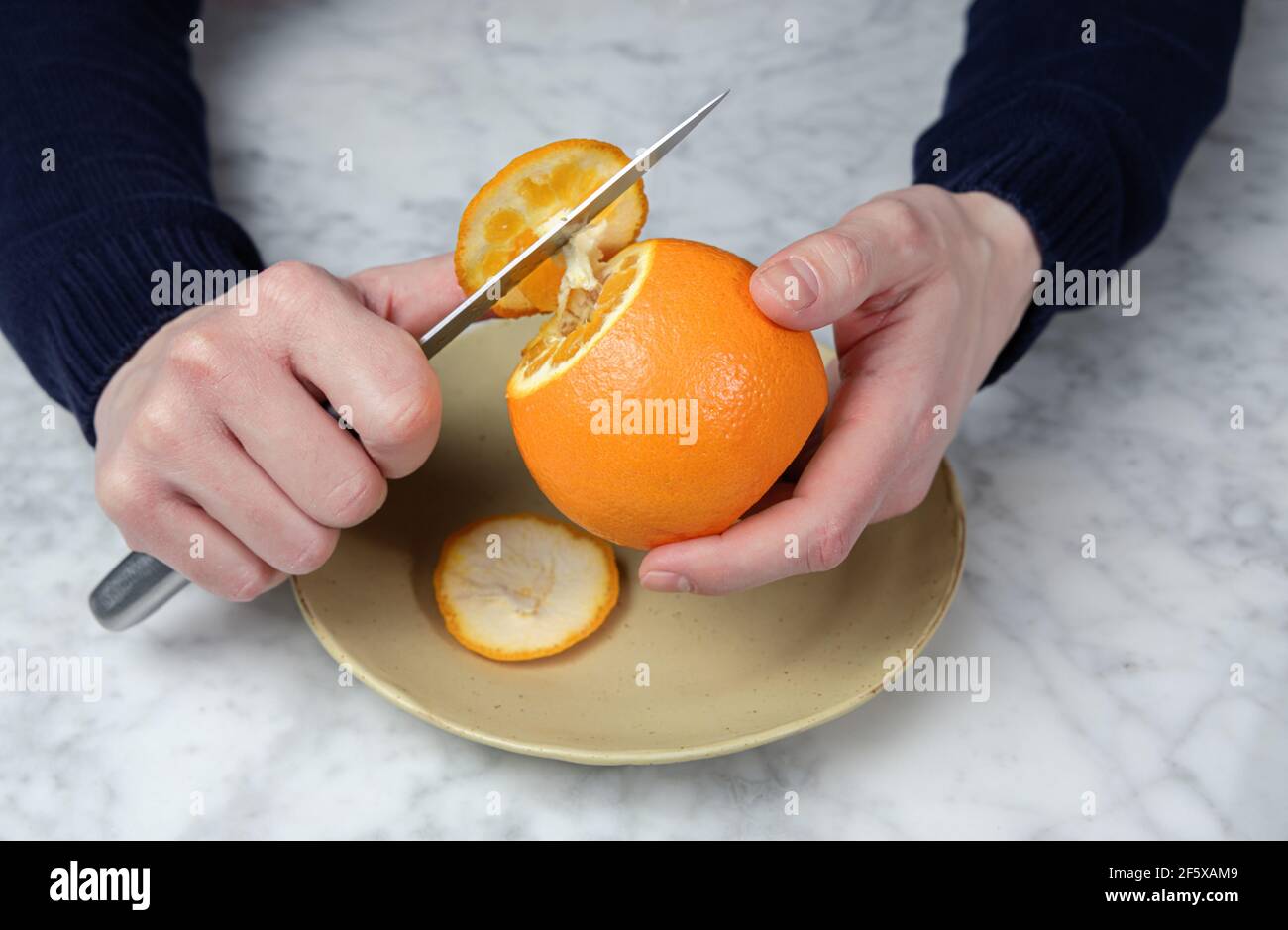 Les mains de l'homme épluchant une orange avec un couteau. Concept d'alimentation saine Banque D'Images