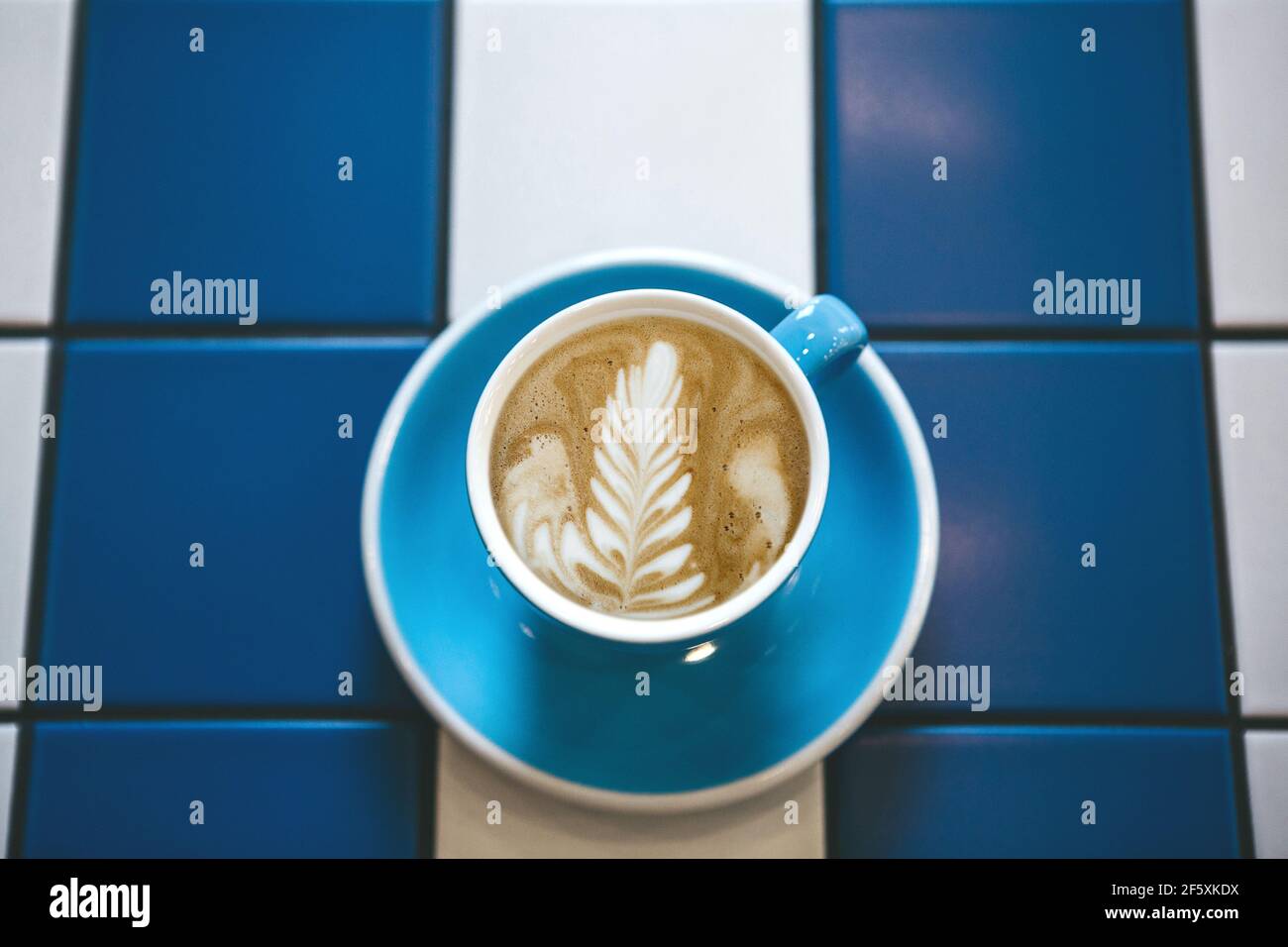 Gros plan de café cappuccino frais et aromatique dans une tasse bleue sur une table de carreaux de céramique bleu et blanc. Banque D'Images