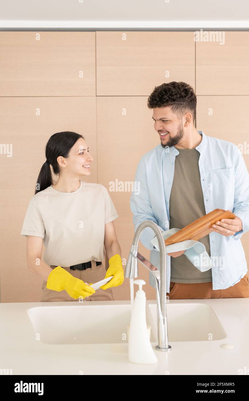 Un jeune homme et une femme heureux se regardant l'un l'autre avec sourit pendant que les femmes lavent la vaisselle et son mari essuyant hacher carte Banque D'Images