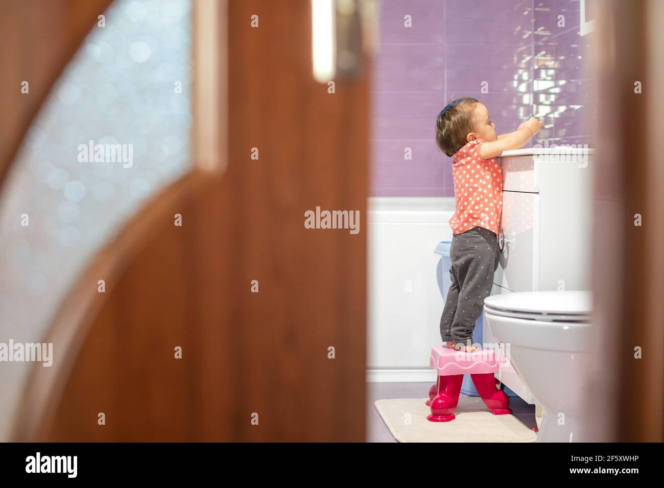 Bébé essayant d'atteindre l'évier pour se laver les mains Banque D'Images