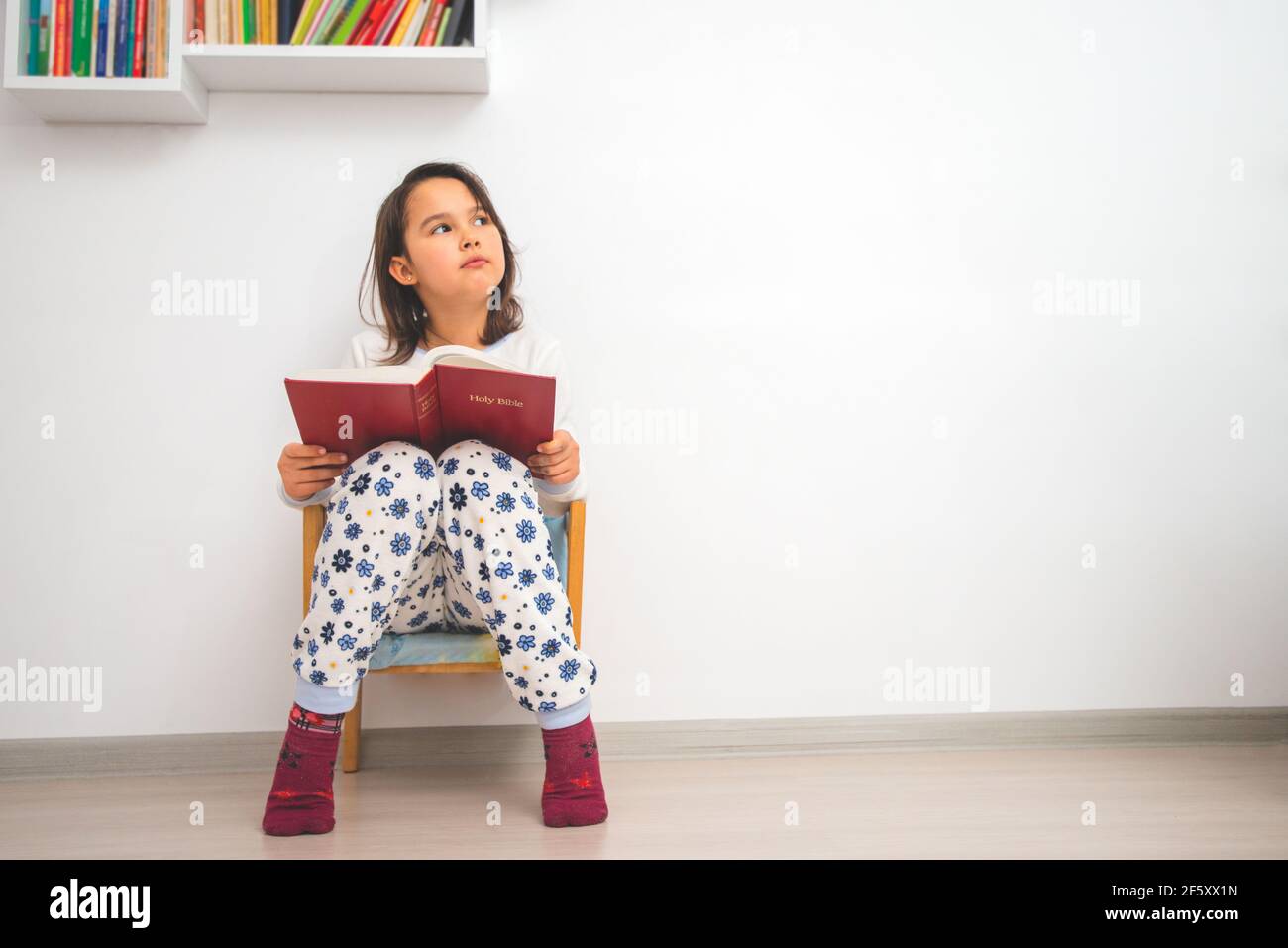 Bonne fille intelligente de lecture de la Bible à côté de la bibliothèque à la maison. Banque D'Images