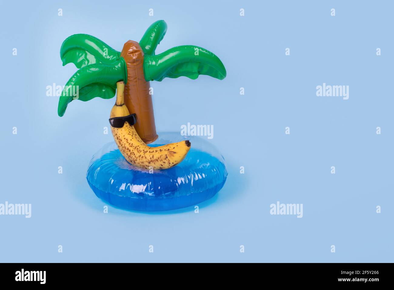 Idée amusante et créative avec une banane dans des lunettes de soleil couchée sur un anneau gonflable de palmier sur un fond bleu. Concept de voyage minimal, style tropical d'été Banque D'Images