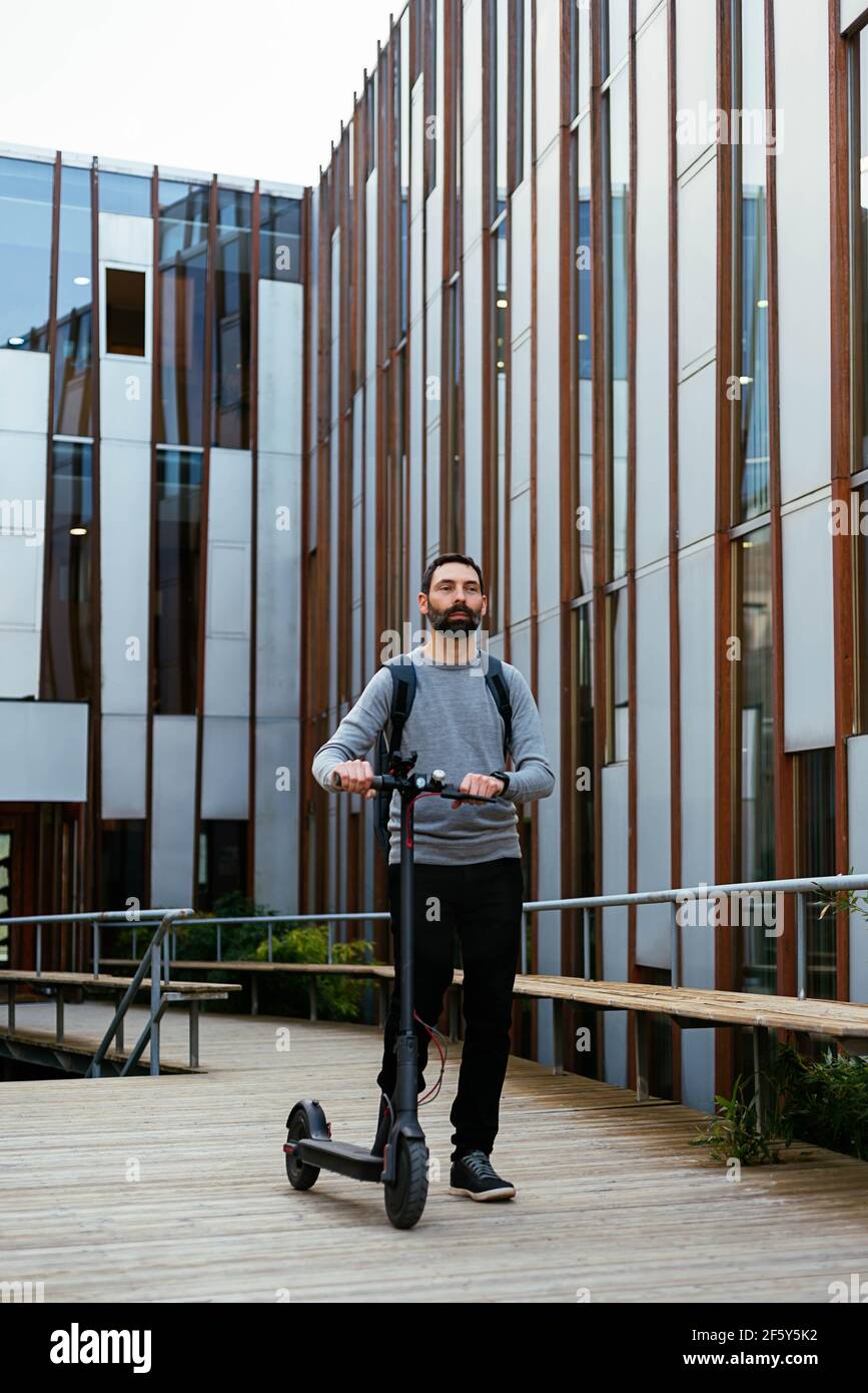 Un jeune homme d'affaires qui se déplace pour travailler à proximité d'un scooter électrique Banque D'Images