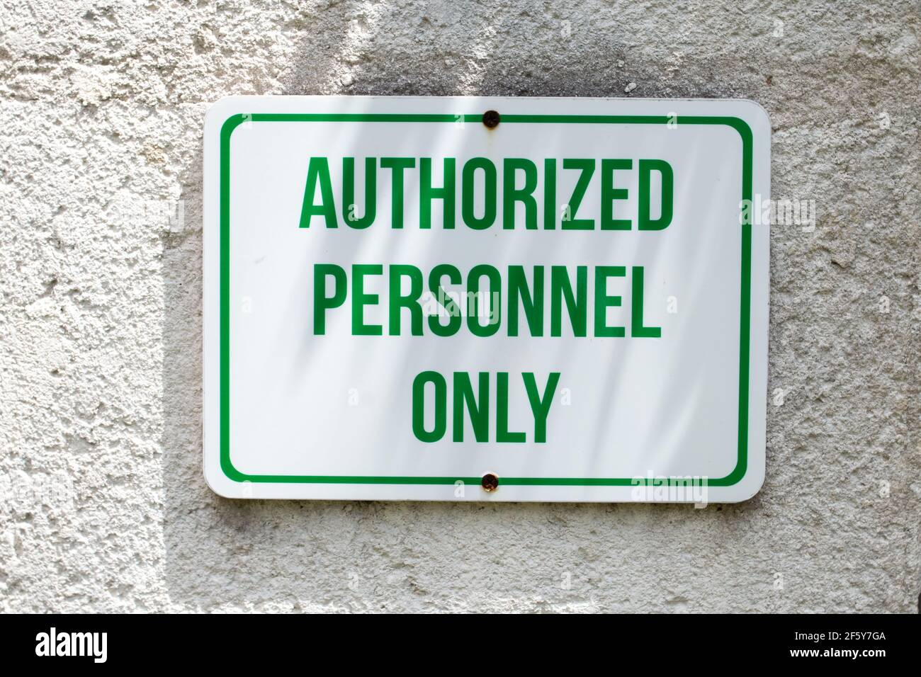 Un panneau rectangulaire blanc avec des lettres majuscules vertes et une bordure verte percée sur un mur en béton indiquant que seul le personnel autorisé peut entrer. Banque D'Images