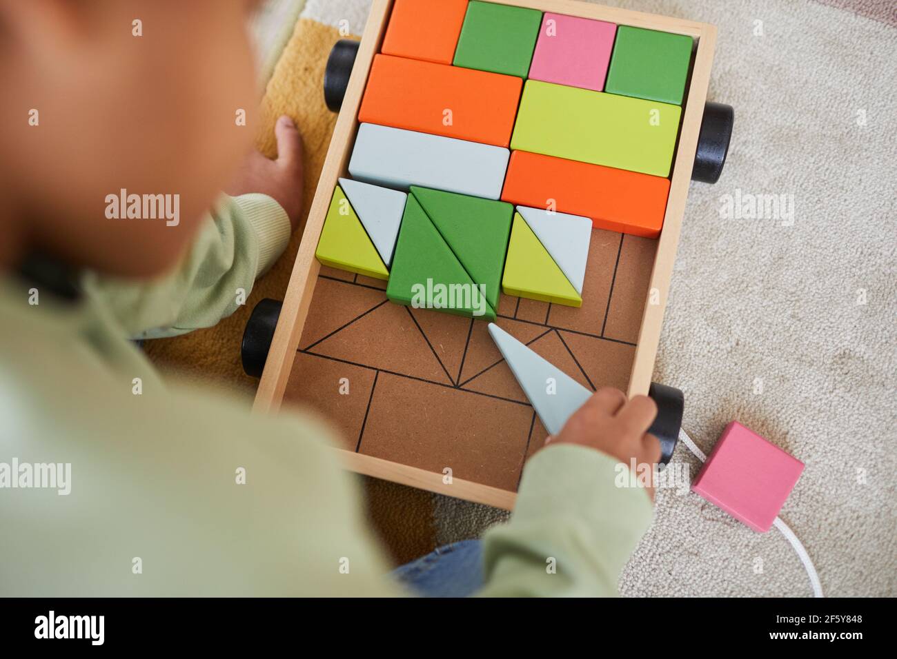 Vue de dessus de gros plan d'un enfant afro-américain méconnu jouant avec des jouets en bois tout en étant assis sur le sol à la maison, salle de copie Banque D'Images